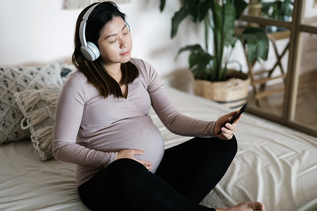 Pregnant woman with headphones on looks at phone