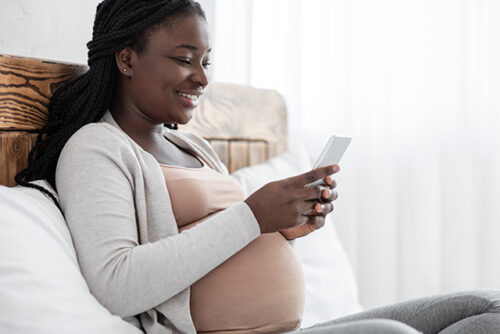 Pregnant woman sits on her bed smiling at her phone