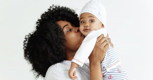 Mother holds up and kisses her baby