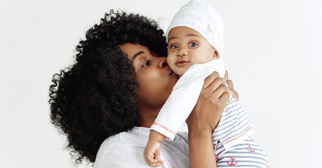 Mother holds up and kisses her baby