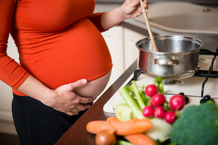 pregnant woman in orange top cooking vegetables on the stove