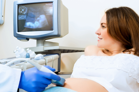 pregnant woman in doctor's office getting ultrasound with baby visible on the screen