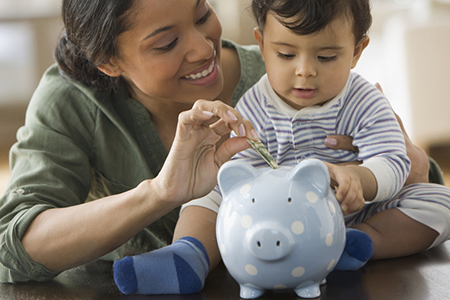 woman with baby son putting money into a piggy bank