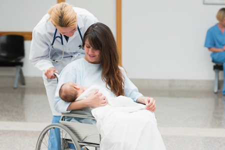 woman in hospital gown in wheelchair holding newborn baby