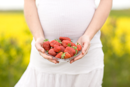 pregnant woman standing in a field holding a bowl of strawberries