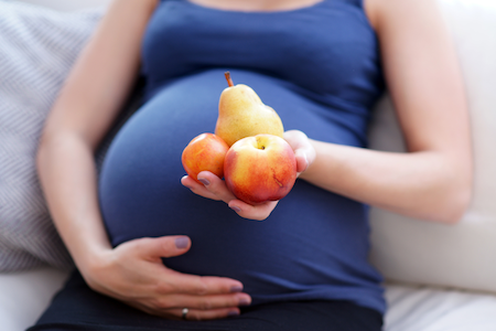 pregnant woman sitting on a couch holding two apples and a pear