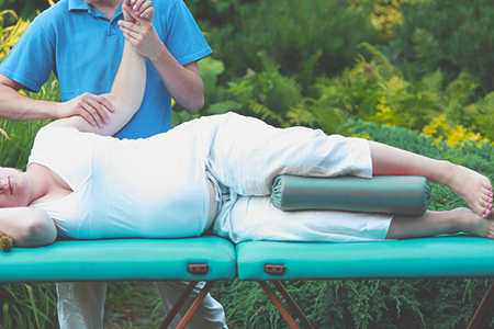 woman laying on a massage table outside, getting a pregnancy massage from a threapist