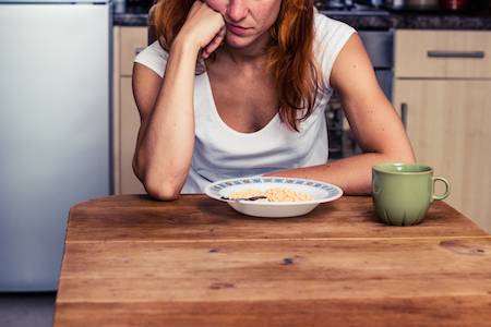 woman sitting at a kitchen table with bowl of cereal, not hungry