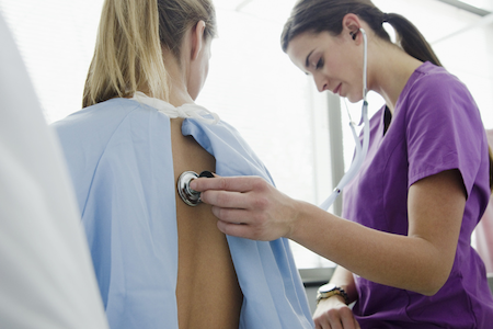 A nurse using a stethoscope to examine a patient who may have PCOS symptoms.