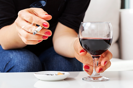 Woman drinking a glass of wine and smoking a cigarette