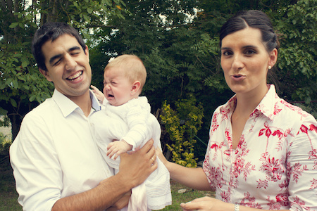 Laughing couple holding their baby at a backyard barbecue
