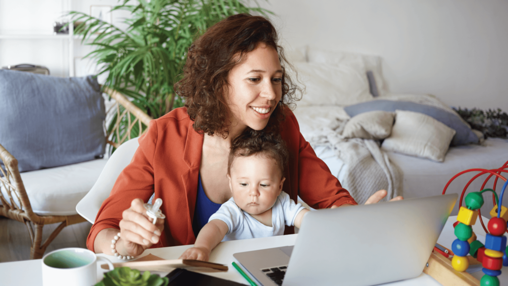 Mother holding baby in her lap as she smiles at laptop.