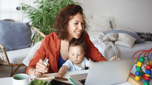 Mother holding baby in her lap as she smiles at laptop.